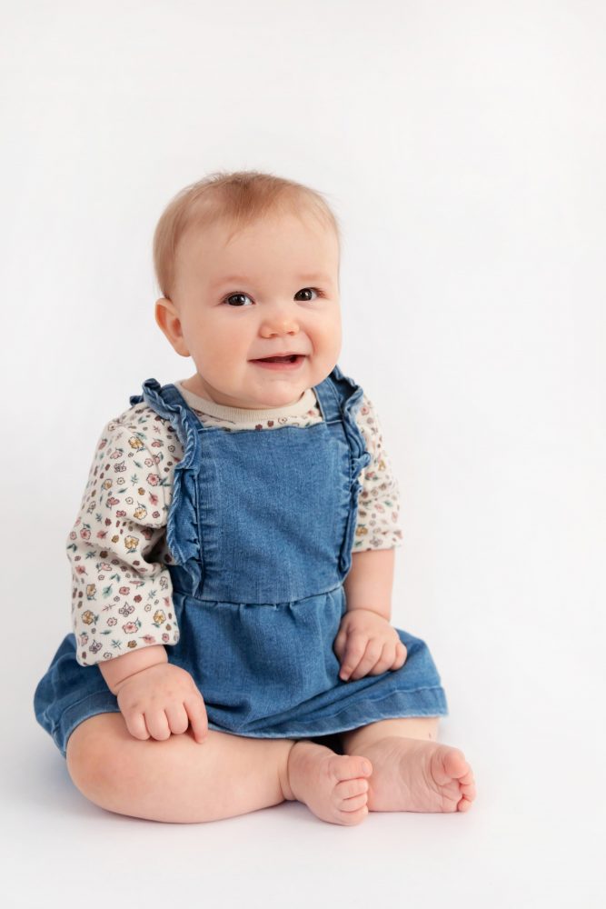 Older brother sitting with baby sister in a studio, smiling and cuddling, neutral white background family portrait