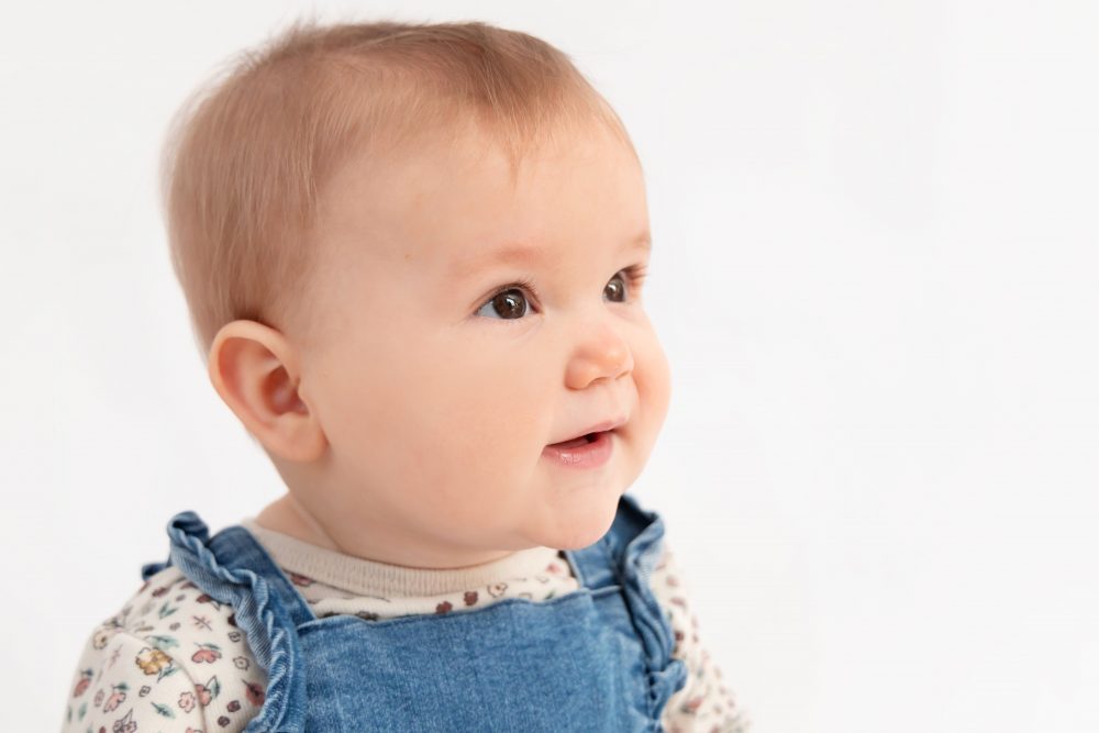 Baby girl in a blue dress crawling and smiling during a studio milestone session on a white backdrop