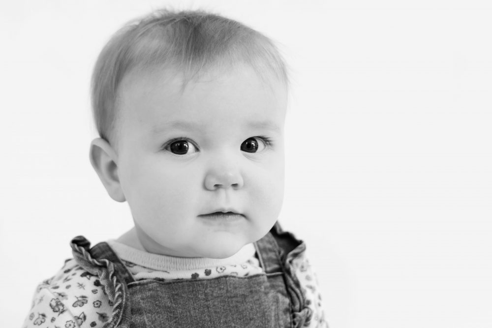Baby girl in a blue dress crawling and smiling during a studio milestone session on a white backdrop