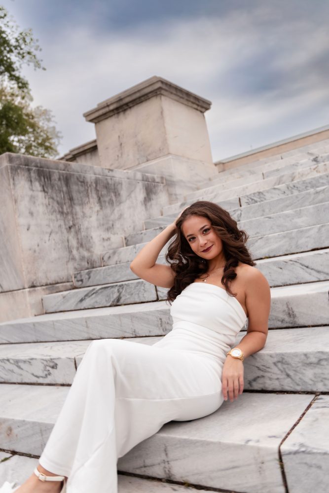 Young woman in an elegant white dress posing in a park at sunset during a graduation photoshoot in Cleveland, Ohio, with soft golden light 