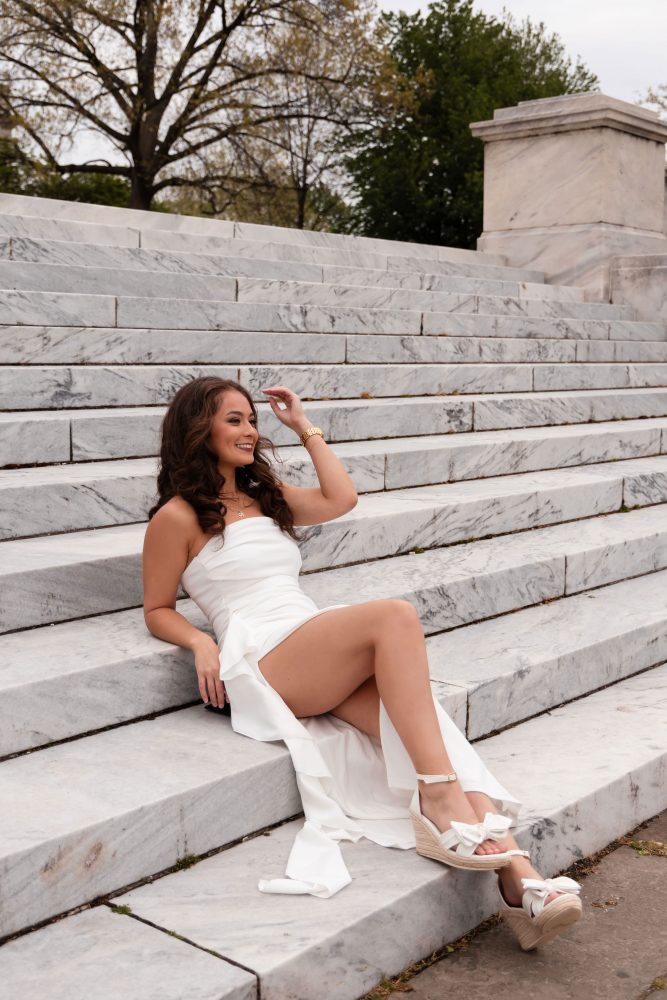 Young woman in an elegant white dress posing in a park at sunset during a graduation photoshoot in Cleveland, Ohio, with soft golden light 