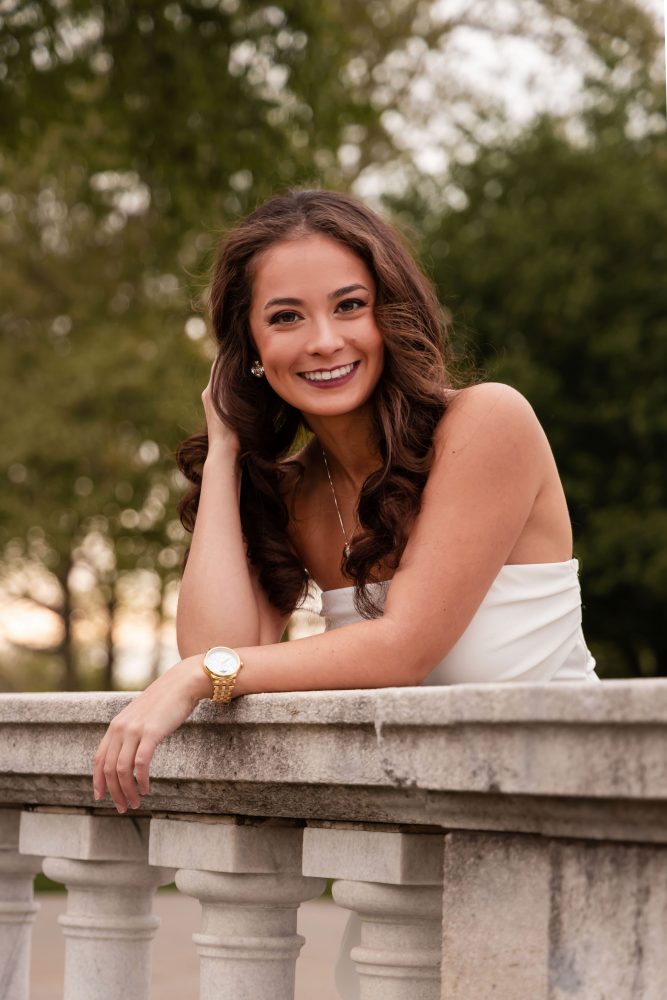 Young woman in an elegant white dress posing in a park at sunset during a graduation photoshoot in Cleveland, Ohio, with soft golden light and trees in the background