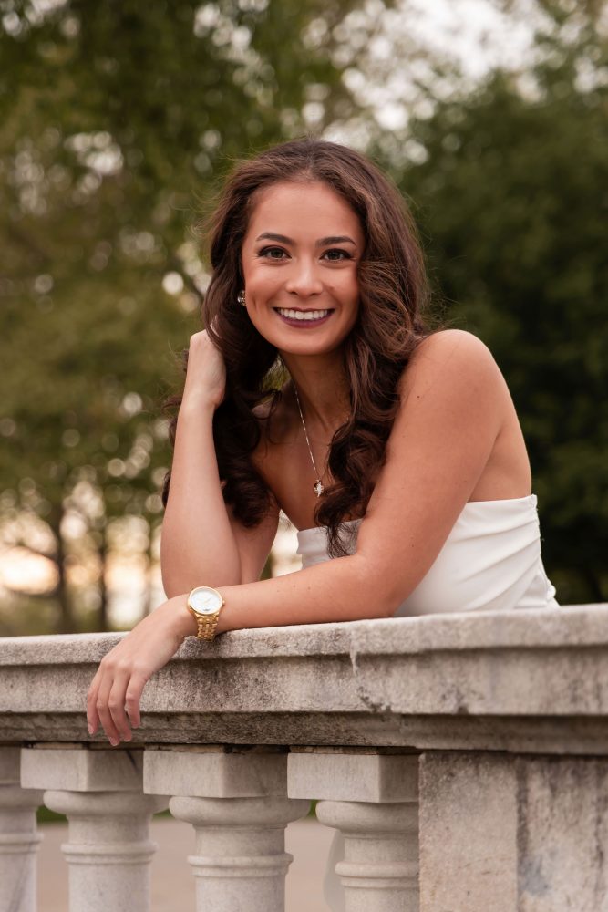 Young woman in an elegant white dress posing in a park at sunset during a graduation photoshoot in Cleveland, Ohio, with soft golden light and trees in the background