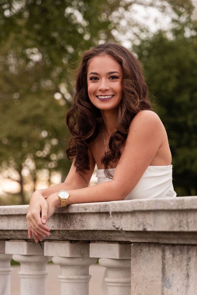 Young woman in an elegant white dress posing in a park at sunset during a graduation photoshoot in Cleveland, Ohio, with soft golden light and trees in the background