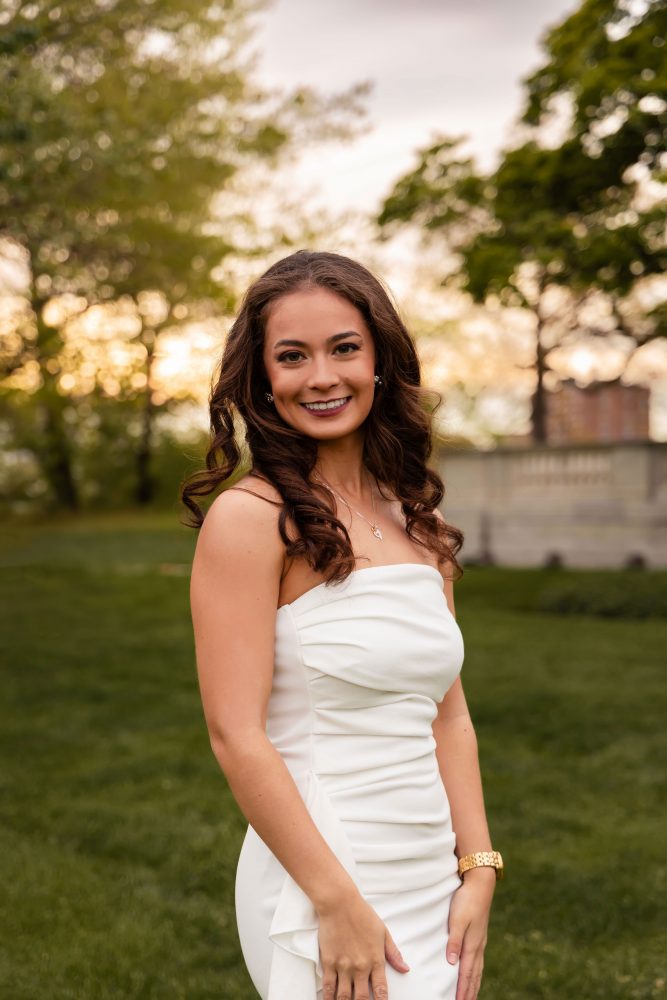 Young woman in an elegant white dress posing in a park at sunset during a graduation photoshoot in Cleveland, Ohio, with soft golden light and trees in the background