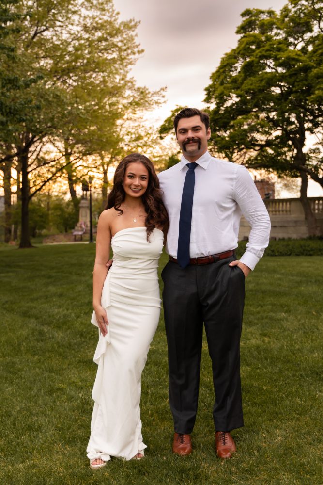 Young woman in an elegant white dress posing in a park at sunset during a graduation photoshoot in Cleveland, Ohio, with soft golden light and trees in the background