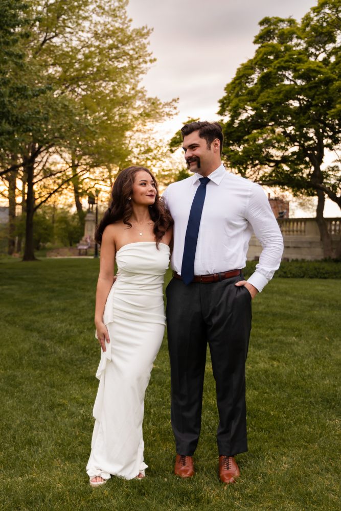 Young woman in an elegant white dress posing in a park at sunset during a graduation photoshoot in Cleveland, Ohio, with soft golden light and trees in the background