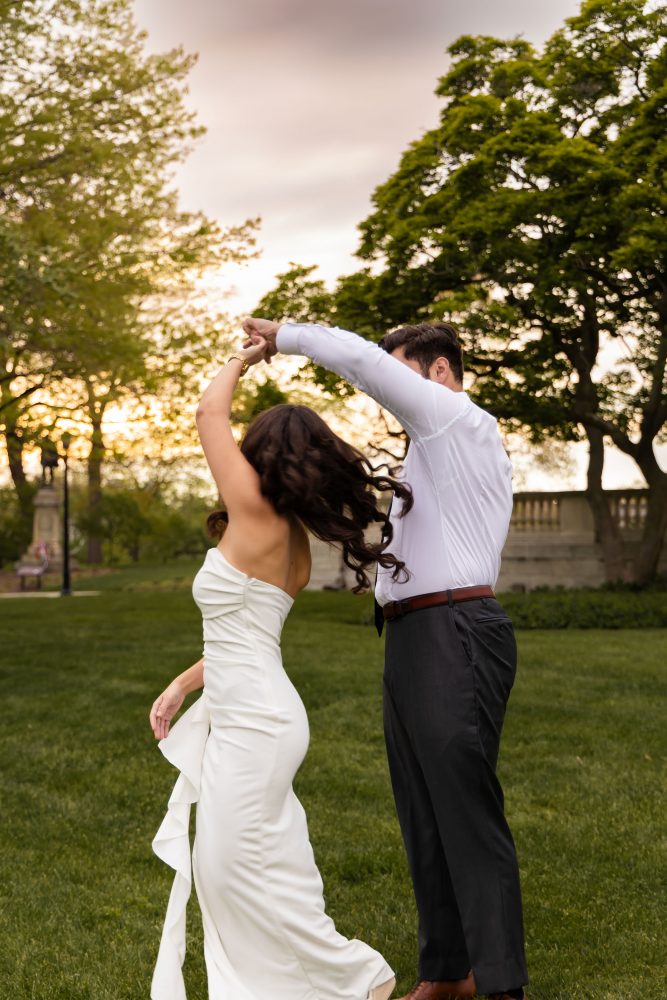 Young woman in an elegant white dress posing in a park at sunset during a graduation photoshoot in Cleveland, Ohio, with soft golden light and trees in the background