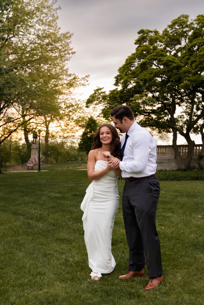 Young woman in an elegant white dress posing in a park at sunset during a graduation photoshoot in Cleveland, Ohio, with soft golden light and trees in the background