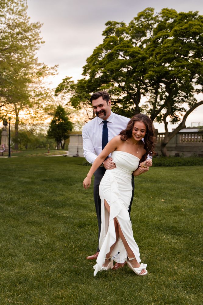 Young woman in an elegant white dress posing in a park at sunset during a graduation photoshoot in Cleveland, Ohio, with soft golden light and trees in the background