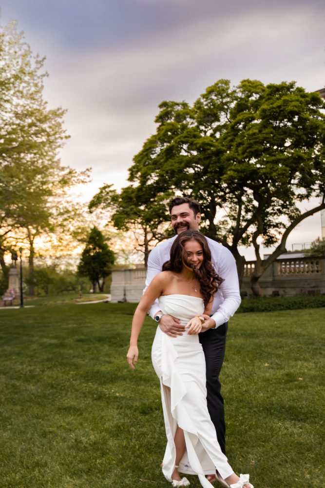 Young woman in an elegant white dress posing in a park at sunset during a graduation photoshoot in Cleveland, Ohio, with soft golden light and trees in the background