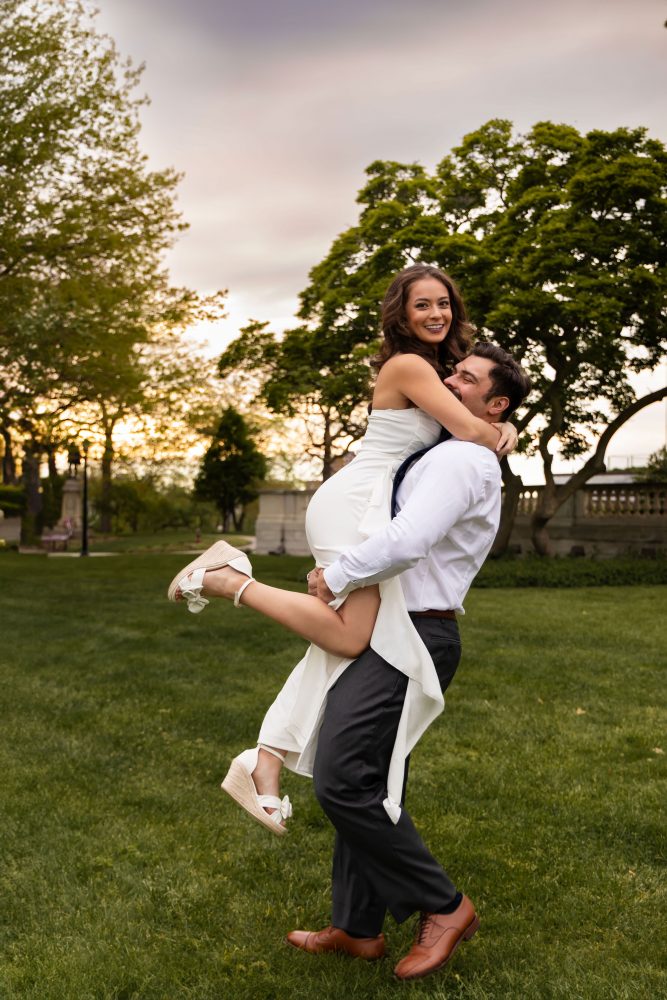Young woman in an elegant white dress posing in a park at sunset during a graduation photoshoot in Cleveland, Ohio, with soft golden light and trees in the background