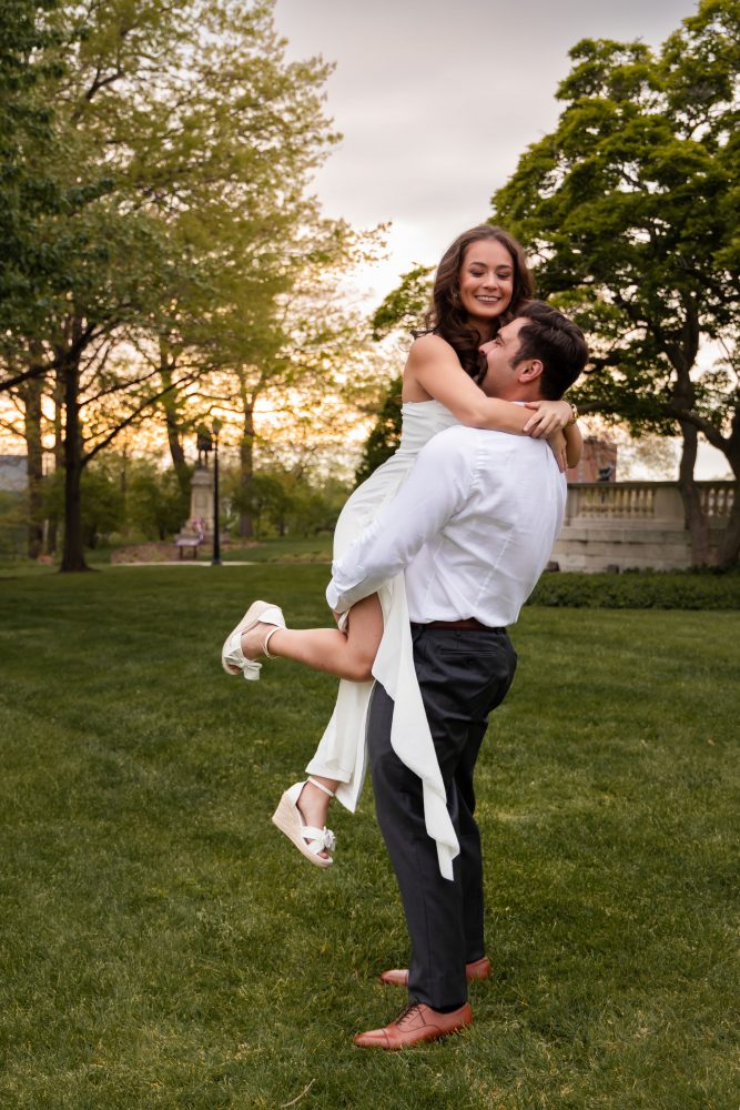 Young woman in an elegant white dress posing in a park at sunset during a graduation photoshoot in Cleveland, Ohio, with soft golden light and trees in the background
