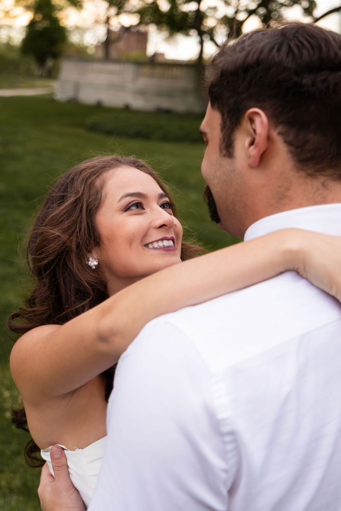 Young woman in an elegant white dress posing in a park at sunset during a graduation photoshoot in Cleveland, Ohio, with soft golden light and trees in the background