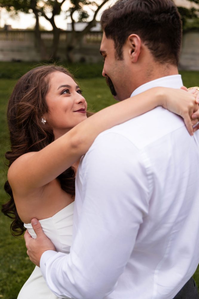 Young woman in an elegant white dress posing in a park at sunset during a graduation photoshoot in Cleveland, Ohio, with soft golden light and trees in the background