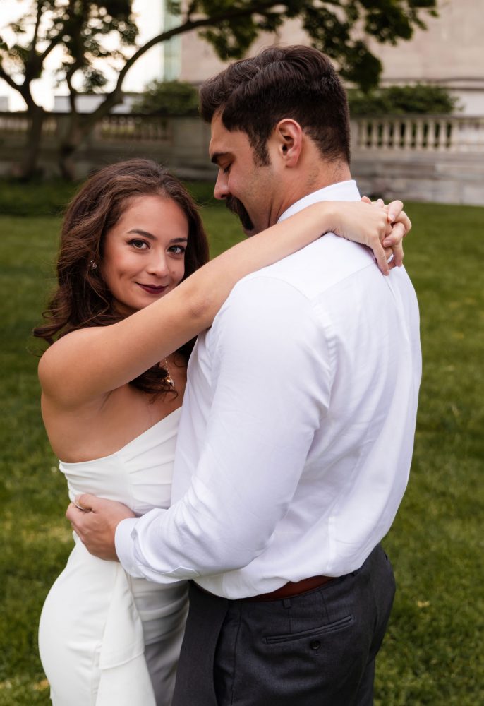 Young woman in an elegant white dress posing in a park at sunset during a graduation photoshoot in Cleveland, Ohio, with soft golden light and trees in the background
