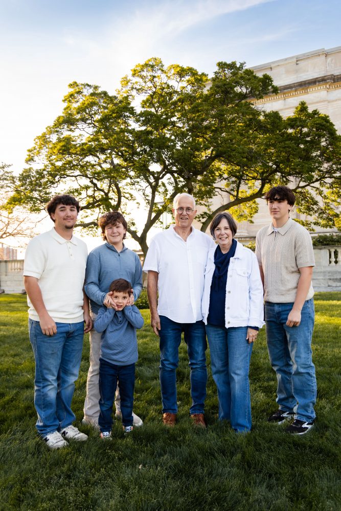 Ten members of an extended family, including grandparents, adults, teenagers, and a young child, walk together across a grassy lawn outside the Cleveland Museum of Art. The group smiles and looks at one another as the museum building and trees appear in the background.