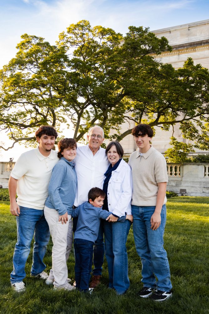 Ten members of an extended family, including grandparents, adults, teenagers, and a young child, walk together across a grassy lawn outside the Cleveland Museum of Art. The group smiles and looks at one another as the museum building and trees appear in the background.