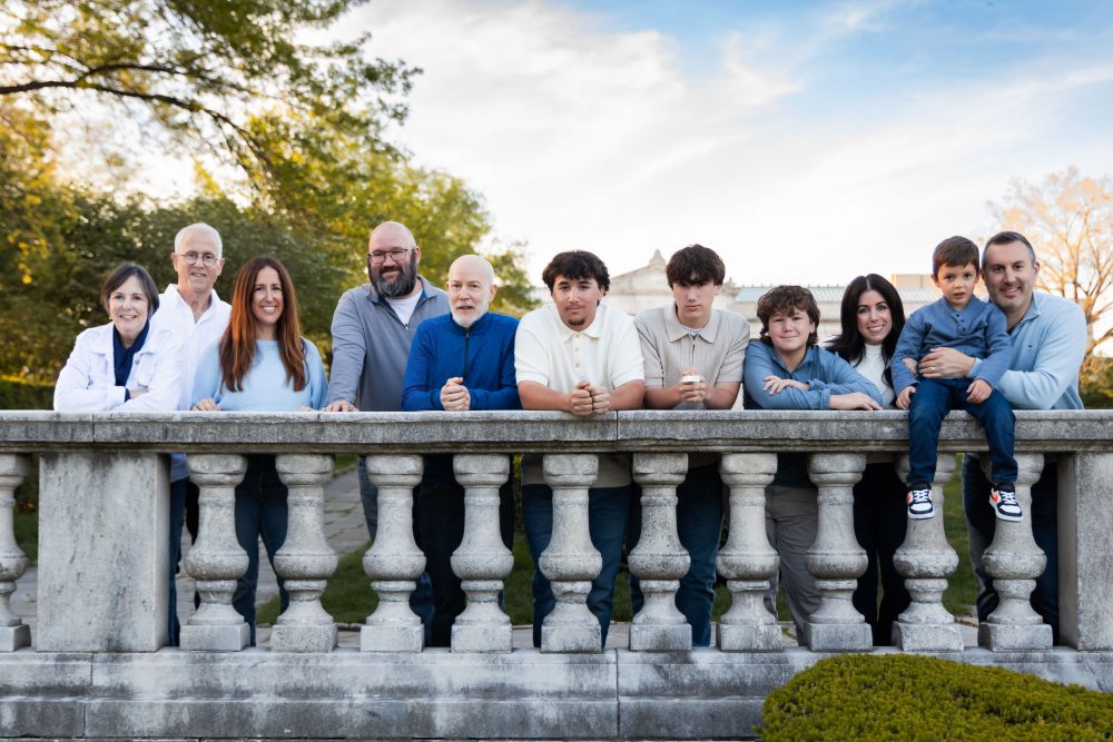 Ten members of an extended family, including grandparents, adults, teenagers, and a young child, walk together across a grassy lawn outside the Cleveland Museum of Art. The group smiles and looks at one another as the museum building and trees appear in the background.