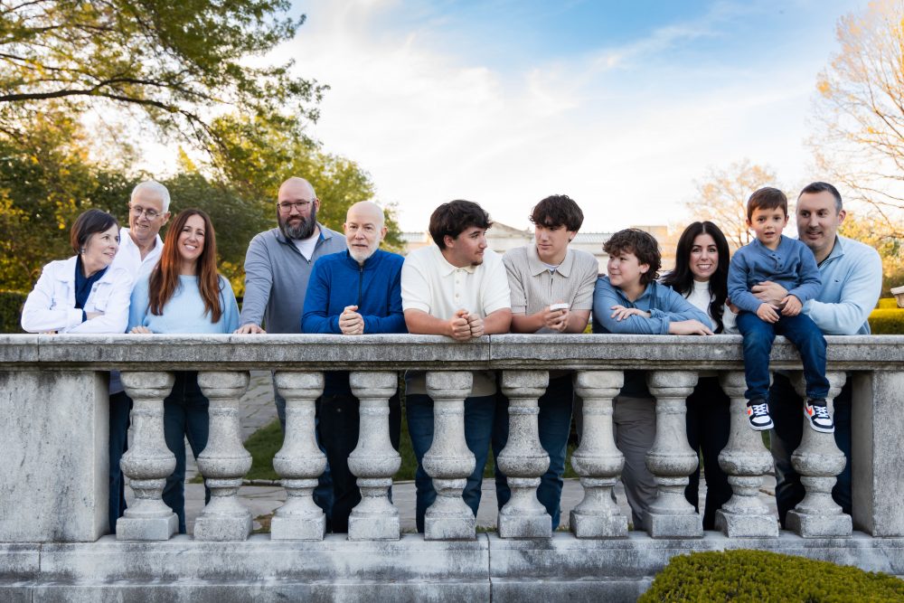 Ten members of an extended family, including grandparents, adults, teenagers, and a young child, walk together across a grassy lawn outside the Cleveland Museum of Art. The group smiles and looks at one another as the museum building and trees appear in the background.