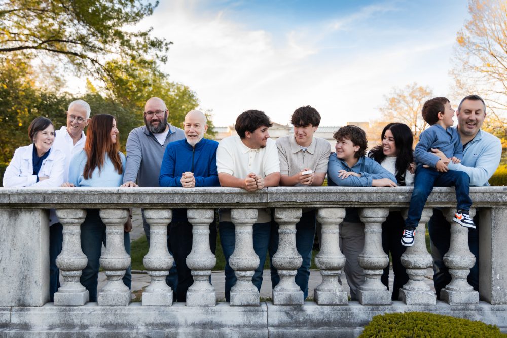 Ten members of an extended family, including grandparents, adults, teenagers, and a young child, walk together across a grassy lawn outside the Cleveland Museum of Art. The group smiles and looks at one another as the museum building and trees appear in the background.
