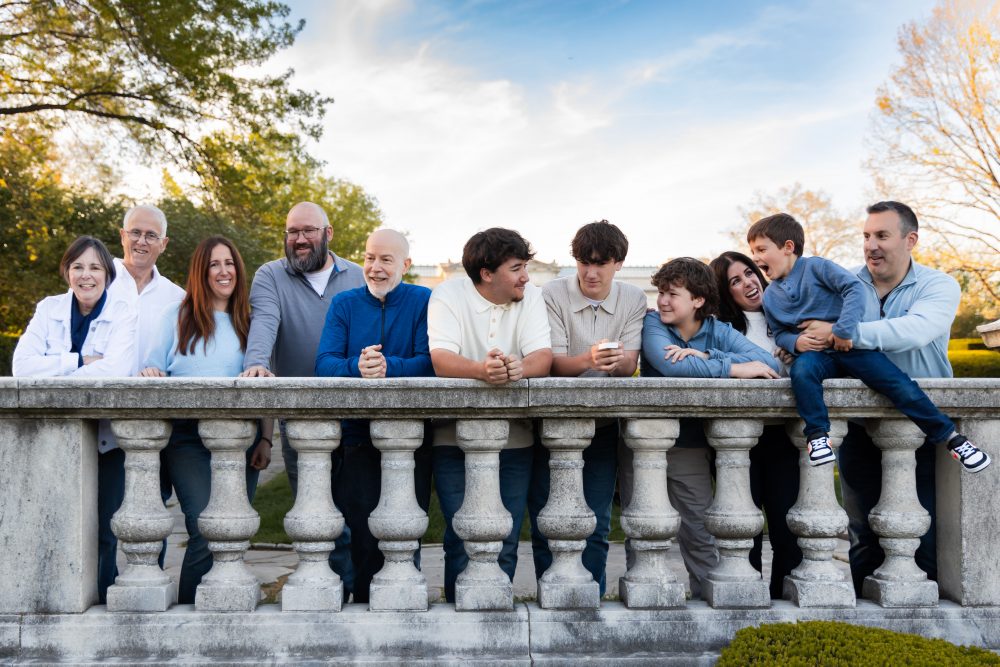 Ten members of an extended family, including grandparents, adults, teenagers, and a young child, walk together across a grassy lawn outside the Cleveland Museum of Art. The group smiles and looks at one another as the museum building and trees appear in the background.