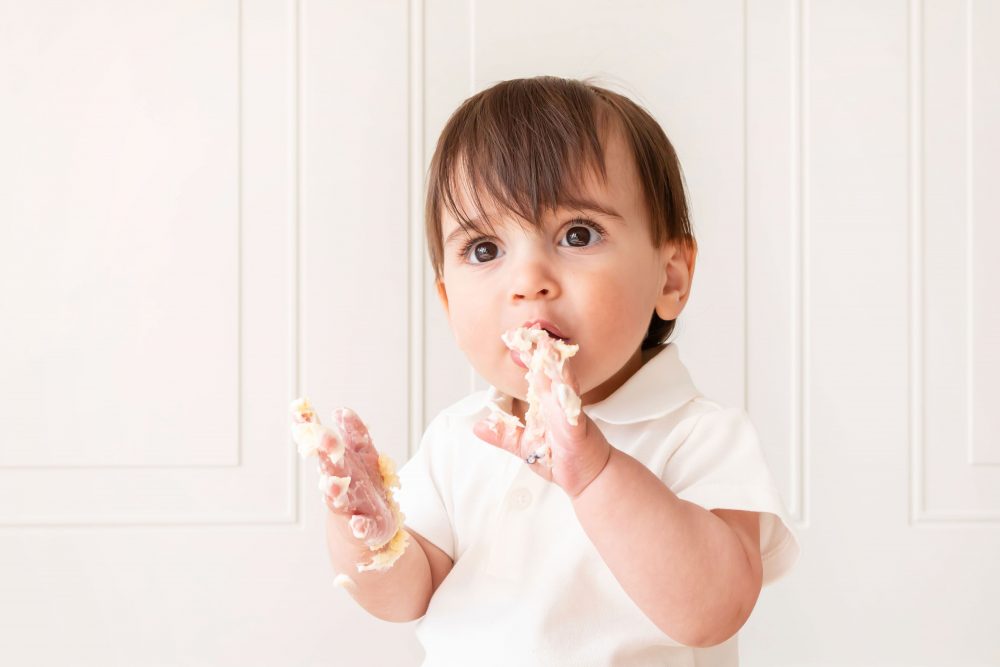 One-year-old baby boy sitting beside a vanilla birthday cake during a classic first birthday cake smash session in Cleveland, Ohio.