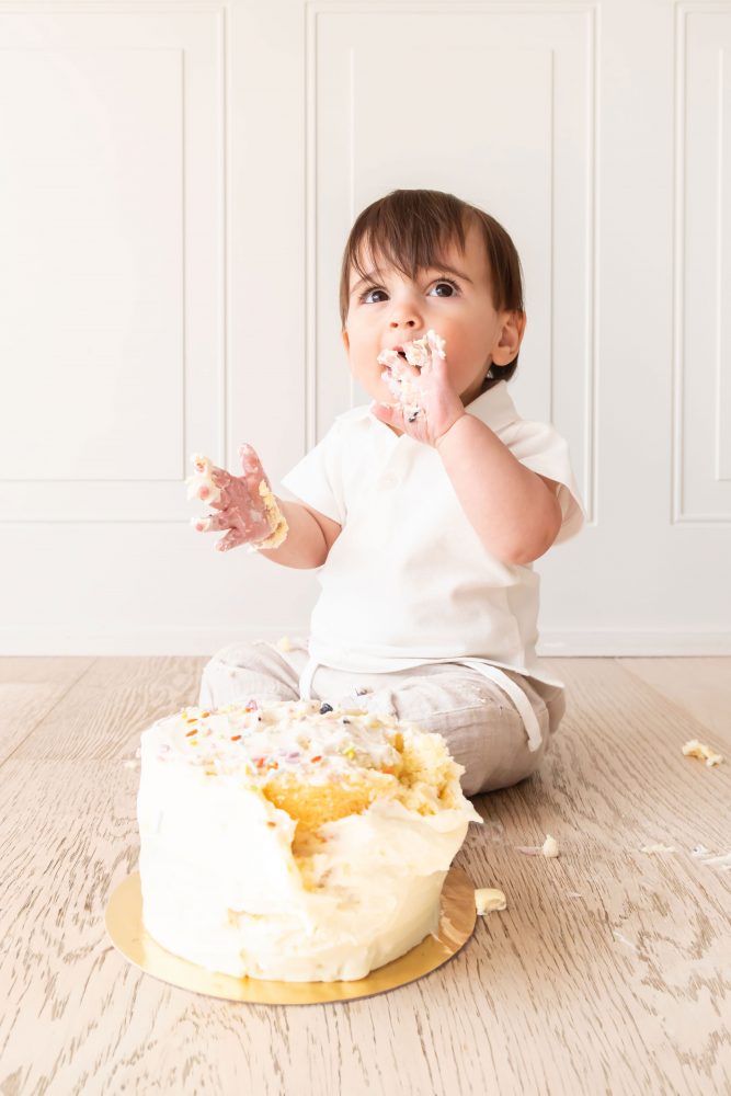 One-year-old baby boy sitting beside a vanilla birthday cake during a classic first birthday cake smash session in Cleveland, Ohio.