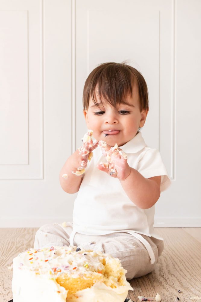Baby boy with frosting on his face smiling during a simple white cake smash photography session by Allison Liffman Photography.