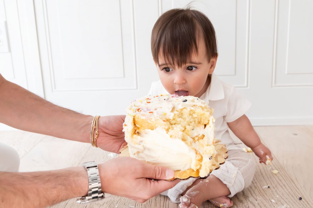 Baby boy with frosting on his face smiling during a simple white cake smash photography session by Allison Liffman Photography.