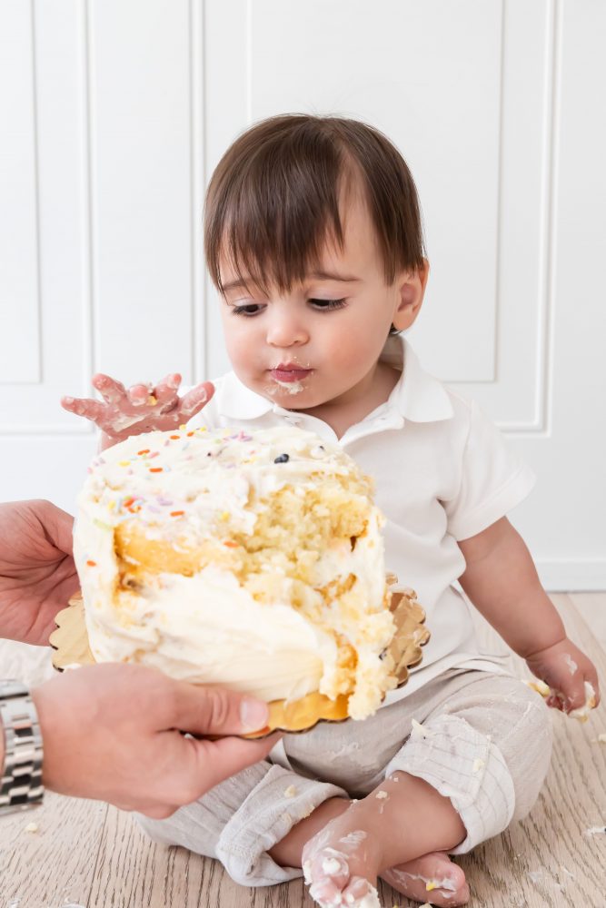 Baby boy with frosting on his face smiling during a simple white cake smash photography session by Allison Liffman Photography.