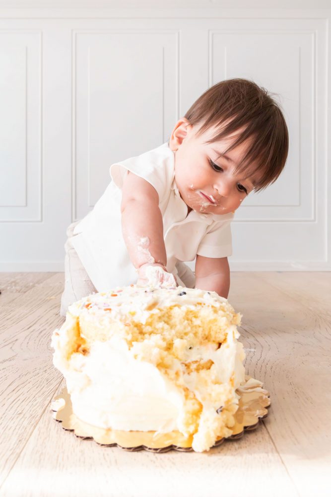 Classic first birthday cake smash featuring a one-year-old boy and vanilla birthday cake in a bright Cleveland photography studio.
