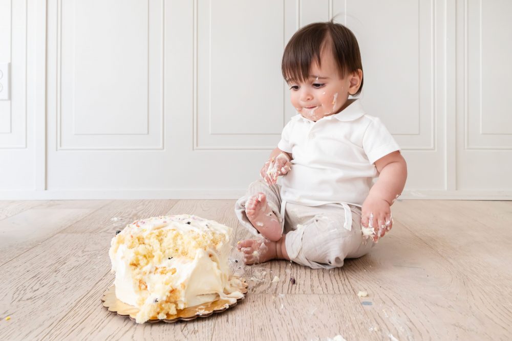 Classic first birthday cake smash featuring a one-year-old boy and vanilla birthday cake in a bright Cleveland photography studio.