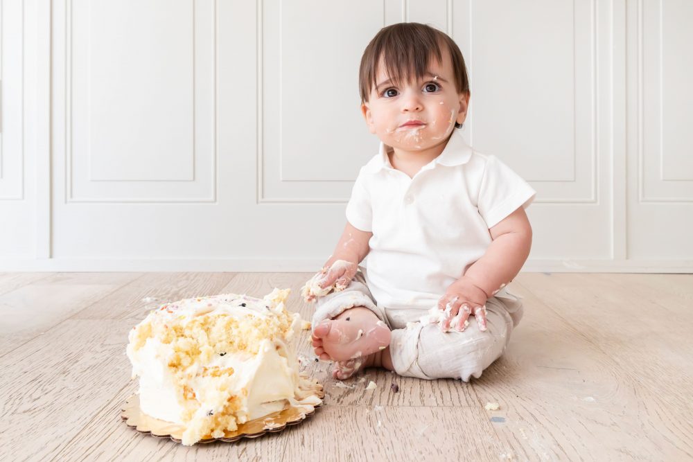 One-year-old baby boy enjoying a classic first birthday cake smash with vanilla frosting during a milestone photography session in Cleveland, Ohio by Allison Liffman Photography.