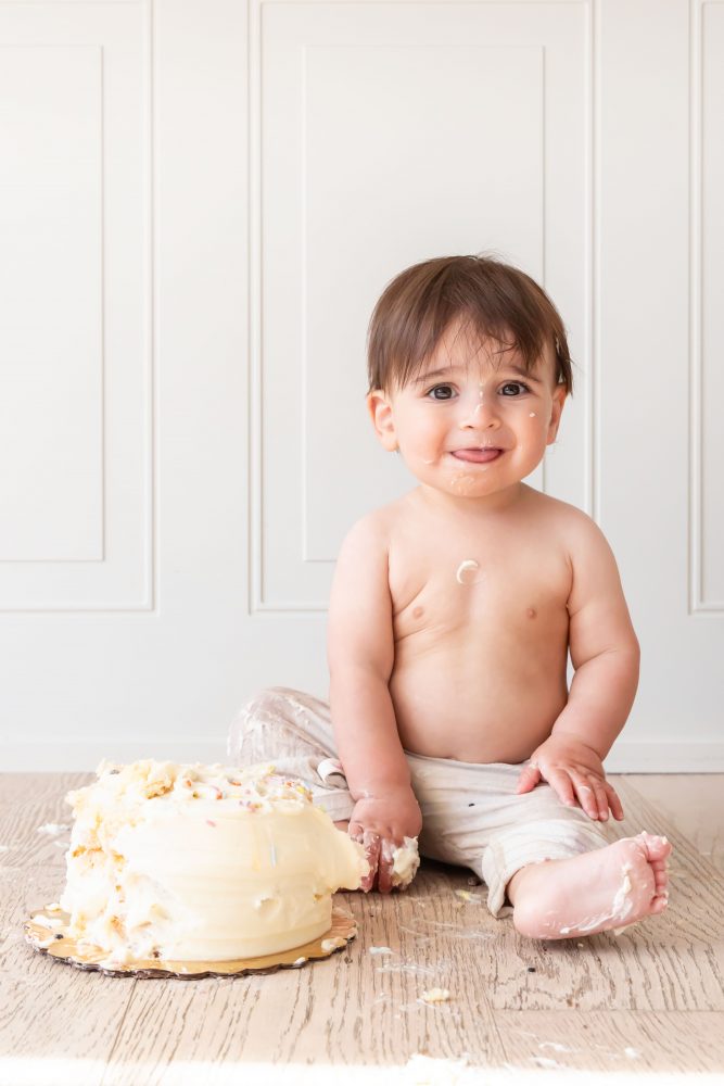 First birthday cake smash photography of a smiling baby boy with frosting-covered hands in Cleveland, Ohio.