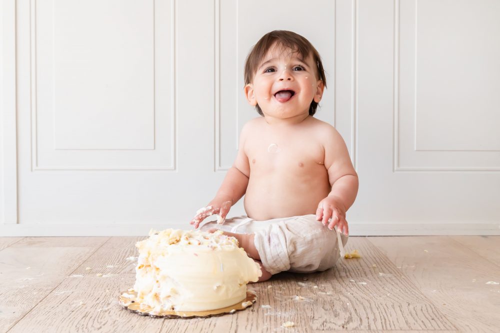 One-year-old baby boy enjoying a classic first birthday cake smash with vanilla frosting during a milestone photography session in Cleveland, Ohio by Allison Liffman Photography.