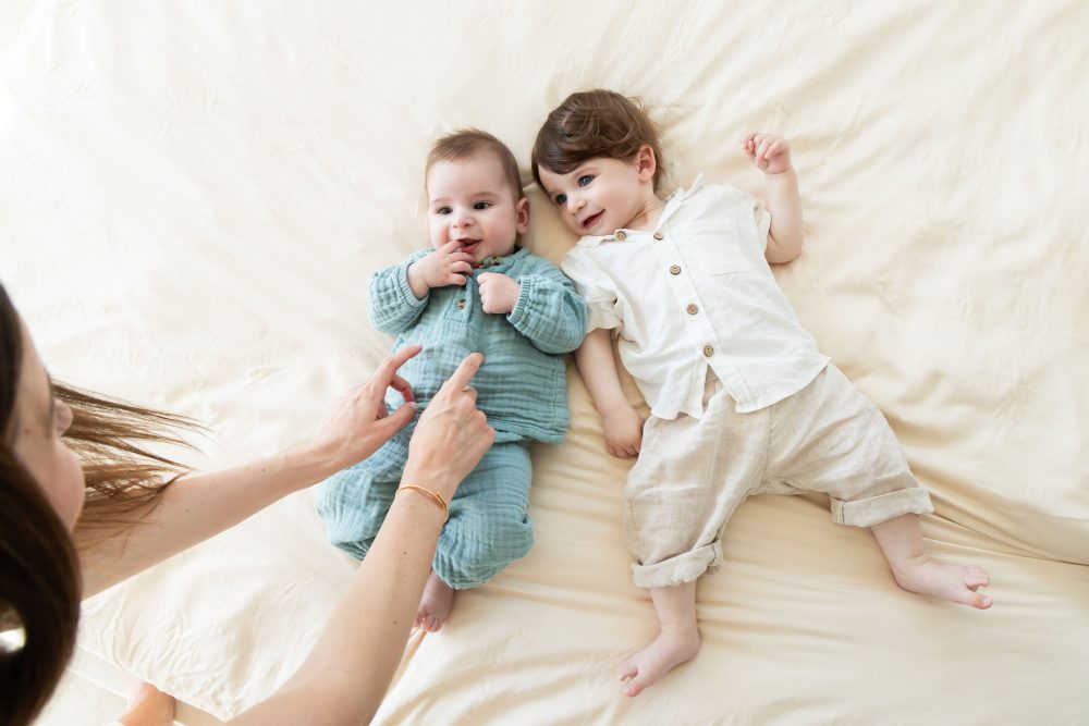 Lifestyle newborn family session in a bright bedroom by a Cleveland family photographer, with parents cuddling their smiling baby on a white bed.