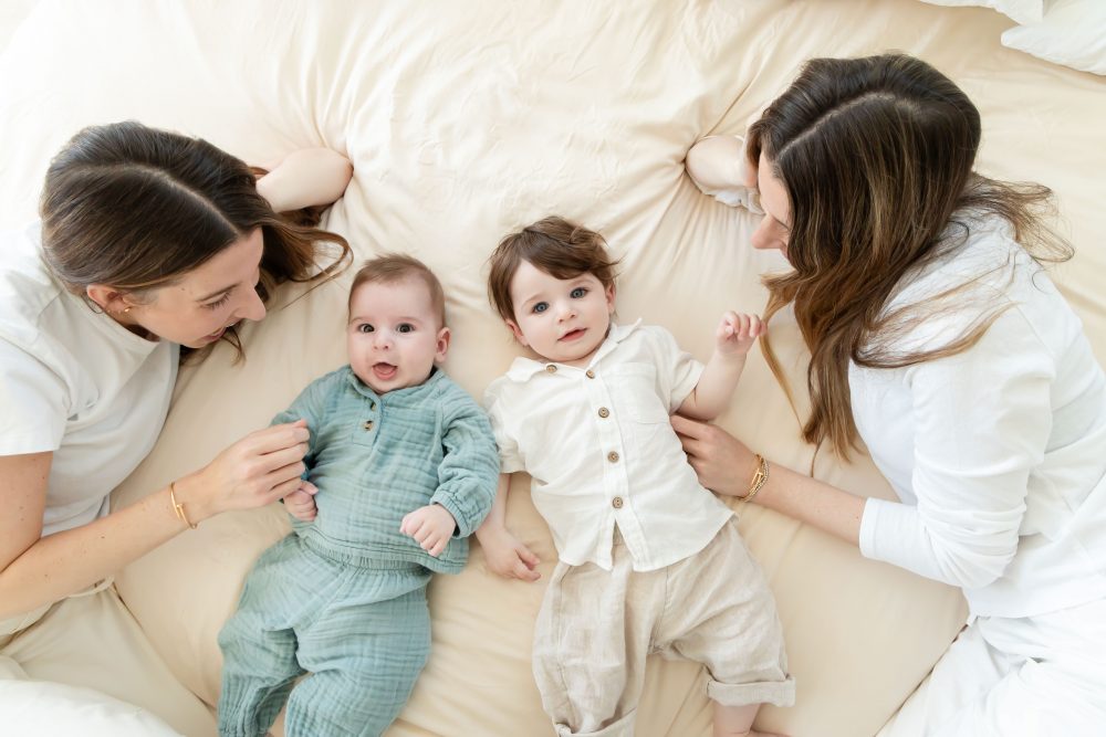 Lifestyle newborn family session in a bright bedroom by a Cleveland family photographer, with parents cuddling their smiling baby on a white bed.