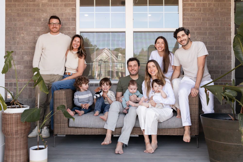 Extended family portrait on a front porch by a Cleveland family photographer, featuring grandparents, parents, young children, a baby, and the family dog.