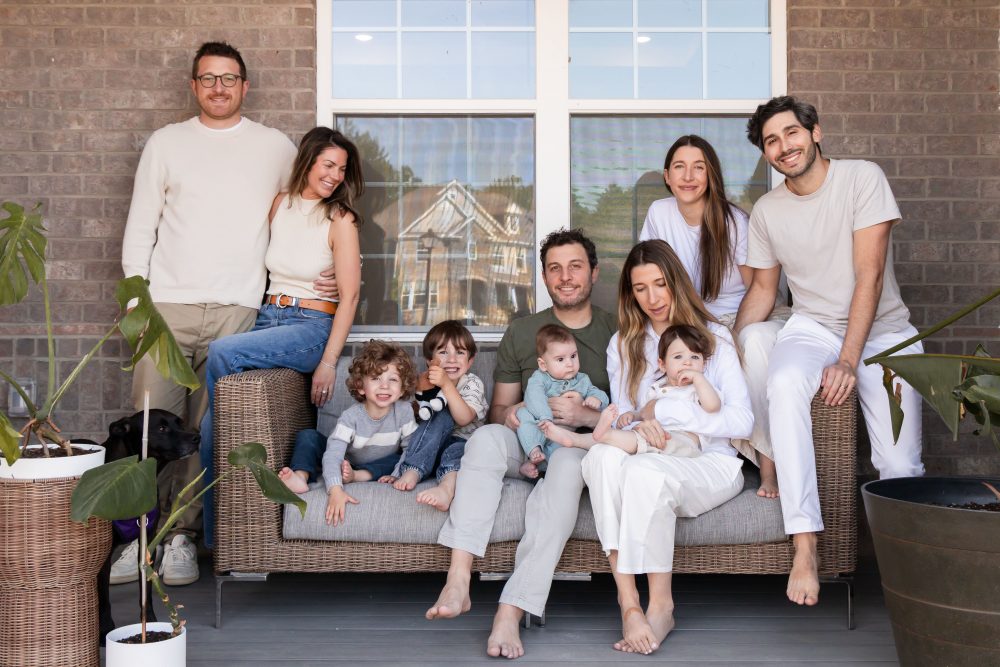Extended family portrait on a front porch by a Cleveland family photographer, featuring grandparents, parents, young children, a baby, and the family dog.