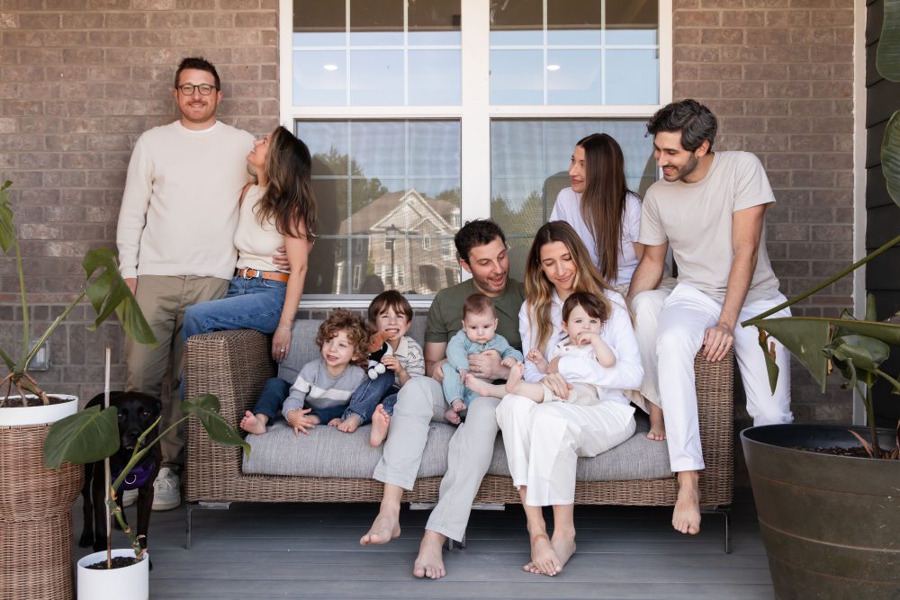 Extended family portrait on a front porch by a Cleveland family photographer, featuring grandparents, parents, young children, a baby, and the family dog.