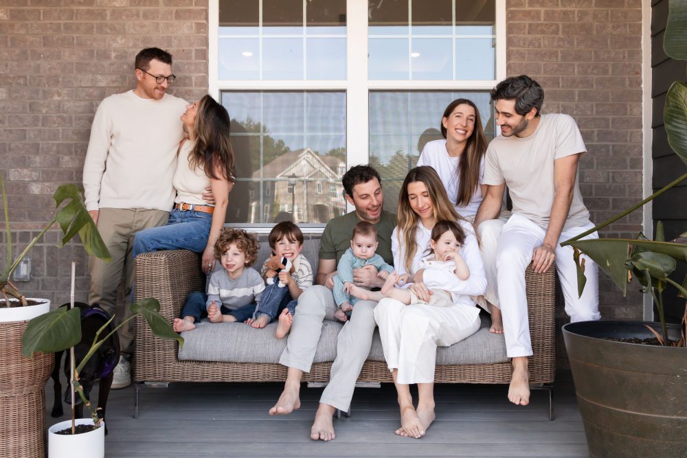 Extended family portrait on a front porch by a Cleveland family photographer, featuring grandparents, parents, young children, a baby, and the family dog.