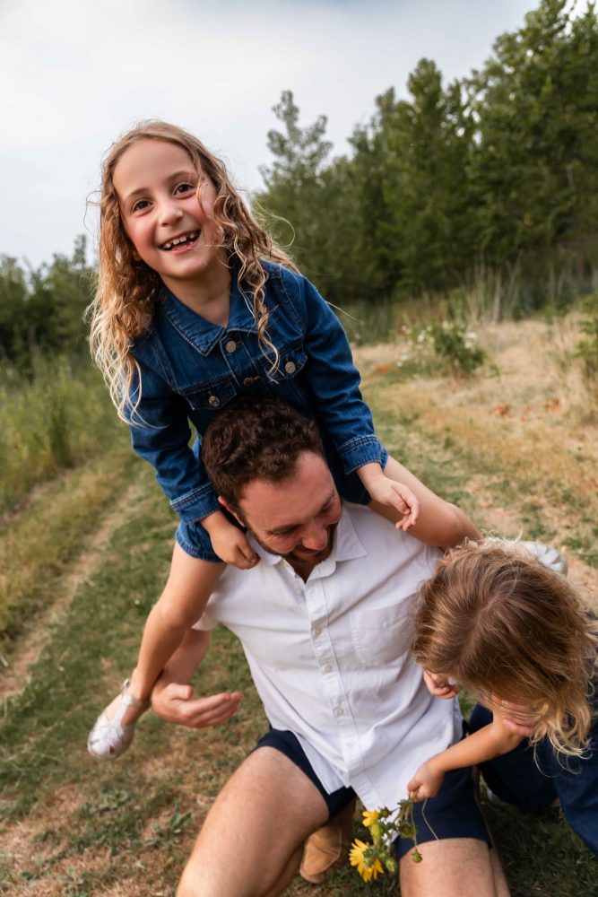 dad playing with his daughters in a field during a Cleveland sunset family photoshoot