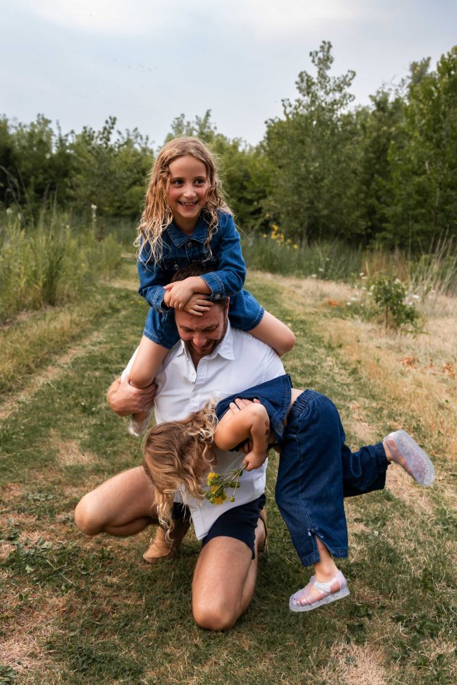 dad playing with his daughters in a field during a Cleveland sunset family photoshoot
