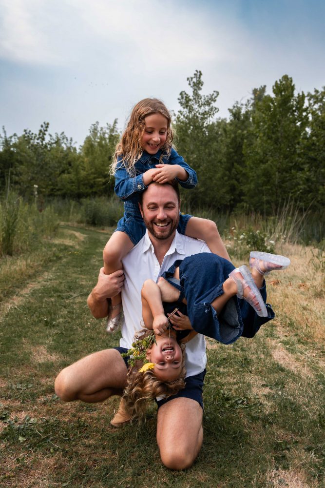 dad playing with his daughters in a field during a Cleveland sunset family photoshoot