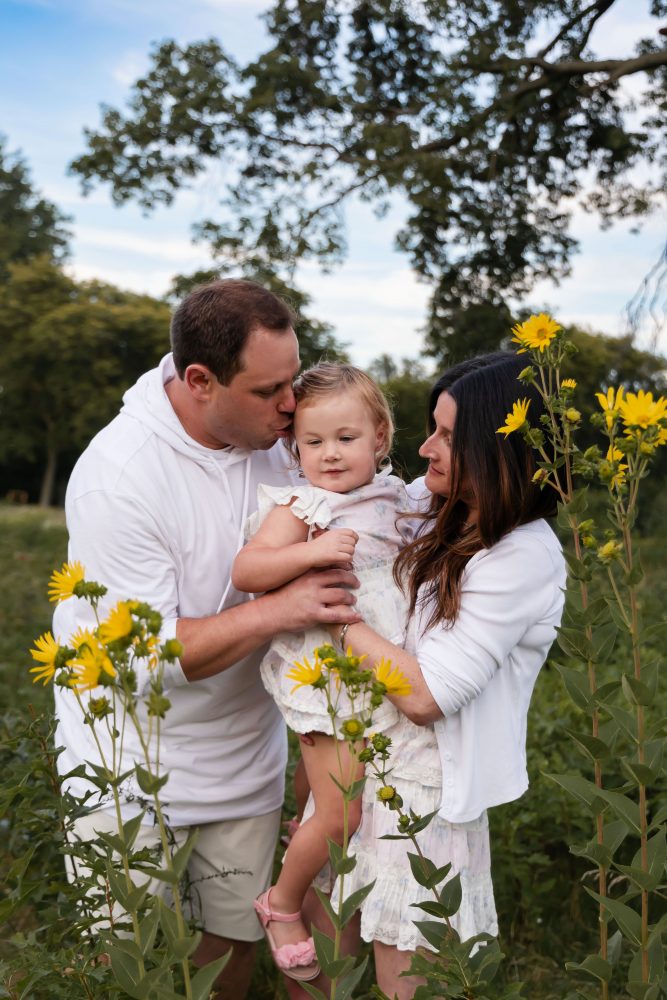 Parents embracing their daughter during a Cleveland family photography session in a wildflower field
