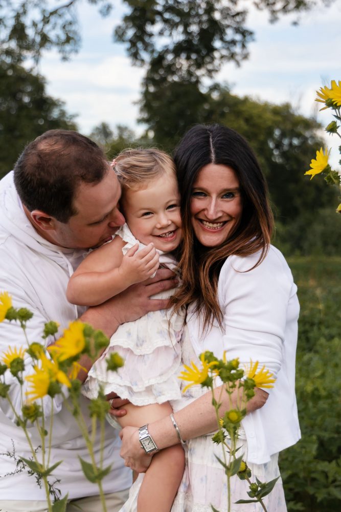 Parents embracing their daughter during a Cleveland family photography session in a wildflower field