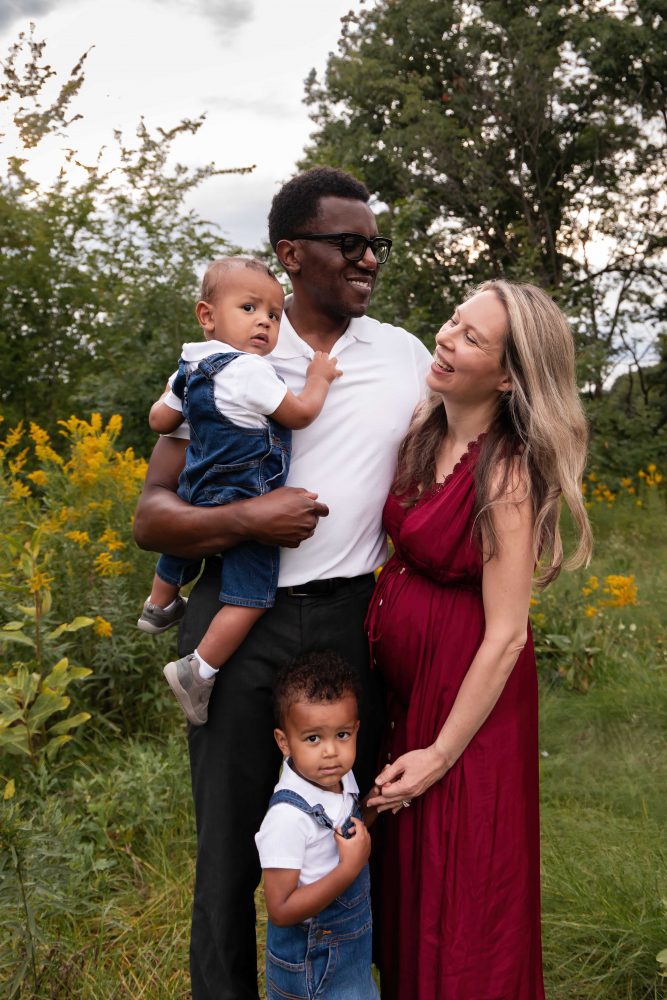 Family of four posing together in a Cleveland wildflower field with dad holding their baby and mom standing beside them.