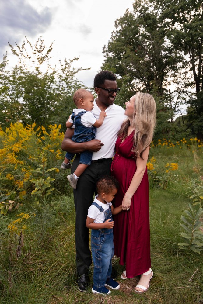 Family of four posing together in a Cleveland wildflower field with dad holding their baby and mom standing beside them.