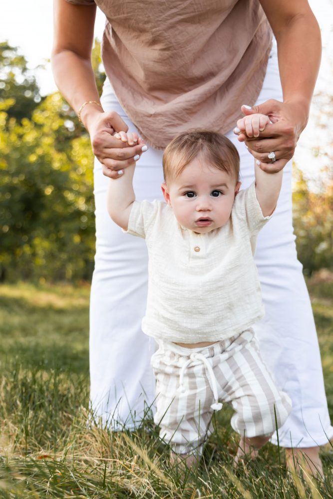 A baby boy standing with his mother's help during an outdoor family photography session in Cleveland, Ohio.